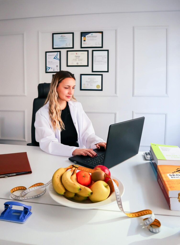 Nutritionist working at desk with laptop and healthy fruits in office setting.